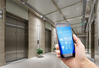 Person holding a smart phone with icons in front of a lift in a hallway