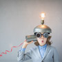 A child inventor, wearing glasses and a strainer as a hat, has a tin can wired to his ear